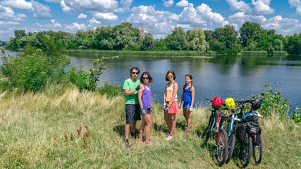 Family on bikes cycling outdoors, active parents and kids on bicycles, aerial view of happy family with children relaxing near beautiful river from above, sport and fitness concept
