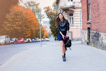 Young fashion woman in casual clothes and black leather jacket over urban city background autumn portrait. Hipster girl posing at street. Fashionable long hair model in elegant autumn clothes.