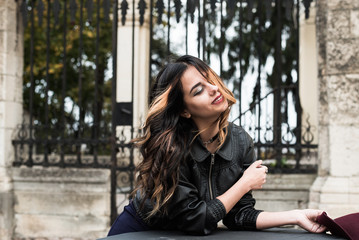 Young fashion woman in casual clothes and black leather jacket over urban city background autumn portrait. Hipster girl posing at street. Fashionable long hair model in elegant autumn clothes.