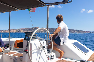 Male skipper navigating the fancy catamaran sailboat on sunny summer day on calm blue sea water....