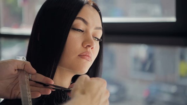 Hairdresser cutting hair of a beautiful serious brunette woman