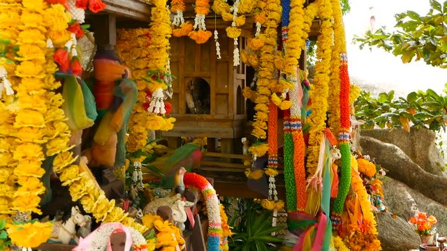 Wooden miniature guardian spirit house. Small buddhist temple shrine, colorful flower garlands. San phra phum erected to bring fortune. Traditional respect animistic rituals, pray ceremonies