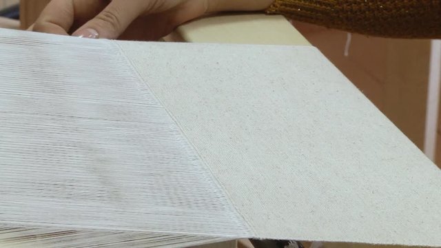 Weaver manually weaves a white linen cloth. Weaver makes a towel by the ancient method. The weaver slides the shuttle through the zev. The weaver passes the shuttle through the warp thread.