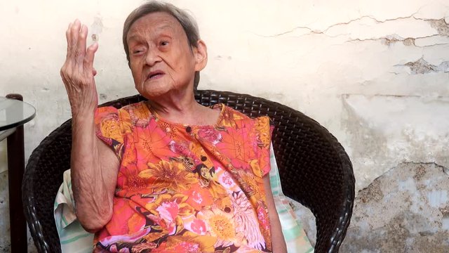90 up of healthy old woman exercising her mind,front view. Portrait of a happy elderly woman in colorful dress counting her fingers and explaining in chinese language,4K video.  