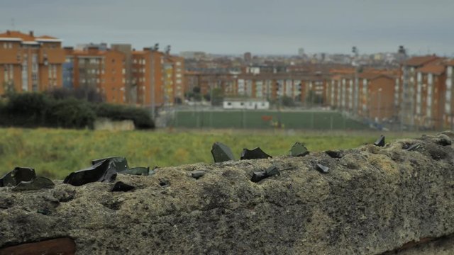 Old stone fence with sharp crashed bottles on the top and city district background
