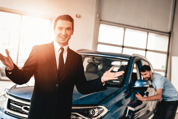 Car Dealer Camera Posing With Buyer On Background.