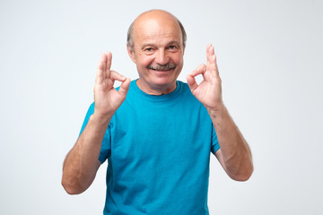 Senior man wearing a blue outfit doing a double ok gesture with his hands.