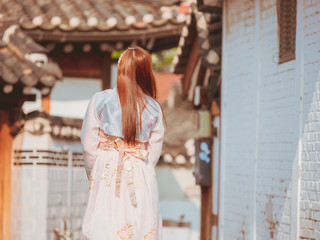 Naklejka premium travel and tourist asia concept from backside long hair woman in korea traditional cloth (hanbok) relax, take picture in vintage town with rim light and soft focus background