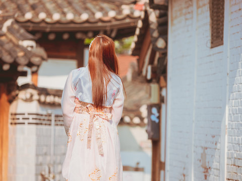 travel and tourist asia concept from backside long hair woman in korea traditional cloth (hanbok) relax, take picture in vintage town with rim light and soft focus background