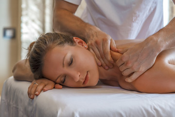 Fototapeta na wymiar Young beautiful Caucasian woman enjoing massage procedure from a pro masseur in hotel spa. Wellness and health tourism and recreation