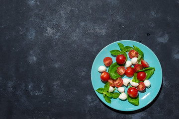 Fresh italian caprese salad with mozzarella and tomatoes on blue plate over dark stone background with copy space, flat lay