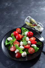 Delicious caprese salad with ripe cherry tomatoes and mini mozzarella cheese balls with fresh basil leaves on black plate and dark slate background. Italian healthy food concept