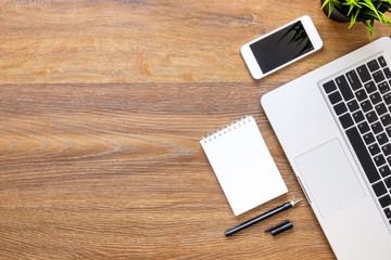 Wood office desk table with notebook, smartphone, laptop and supplies. Top view with copy space, flat lay.