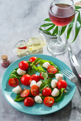 Caprese salad. Healthy meal with cherry tomatoes, mozzarella balls, spices, fresh rocket and basil with red wine on slate background . Concept for a tasty and healthy vegetarian meal.
