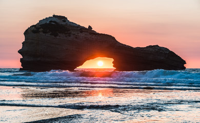 Sunset on a beach in Biarritz with the sun in the center of a rock's hole. Basque country of France. - obrazy, fototapety, plakaty