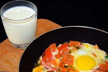 Egg with tomatoes, green onions and cheese. Glass of steamed milk. White plate on black background. Rich protein Breakfast. Food for athletes. Diet menu. Omelet with cheese for dinner. Slices of chees