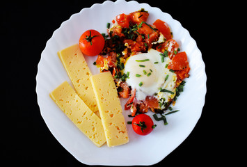 Egg with tomatoes, green onions and cheese. White plate on black background. Rich protein Breakfast. Food for athletes. Diet menu. Omelet with cheese for dinner. Slices of cheese and cherry tomatoes o