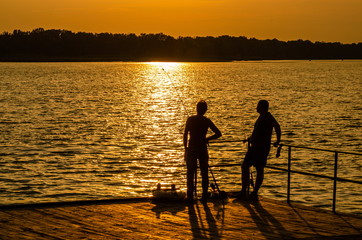 Silhouettes of fishermen against the background of summer sunset.