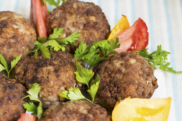 Homemade meat cutlets close-up on a plate with tomatoes and greens.