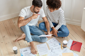 Top view of mixed race woman and man sit together on floor, prepare for upcoming exams, dressed in...