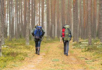 Man with a backpack and beard and his friend hiking in forest in autumn.