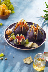 baked figs with goat cheese,walnuts and honey on ceramic plate and blue concrete background, selective focus