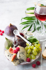 delicacy blue cheeses, fruit and jam in jar with red wine in glass on white stone background, copy space