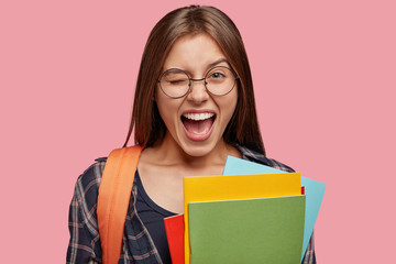Isolated shot of optimistic Caucasain girl blinks eyes, opens mouth widely, has fun together with...
