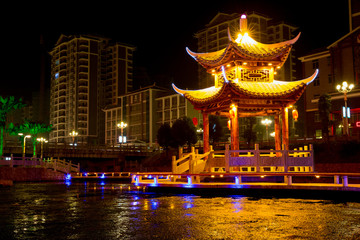Chinese Pagoda at night time, City Architecture, China Culture/Tourism. Multi-Color Lights, lake with calm water. Skyscrapers in the background, City Landmark. Chinese Traditional Architecture