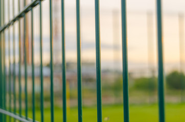 Fencing of the football field from metal with a green lawn.