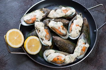 Serving pan with kiwi mussels baked in cheese sauce, studio shot on a grey stone surface