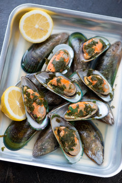 Oven-tray with green mussels stewed in white wine with parsley, elevated view, closeup