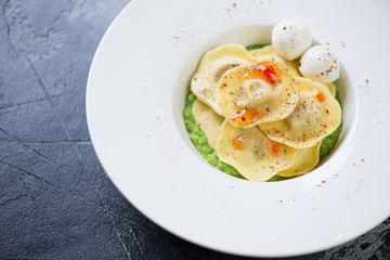 White plate with italian ravioli on a bedding of green peas puree, grey concrete background, close-up