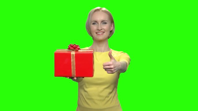 Happy middle aged woman with red gift box and thumb up. Green hromakey background for keying.