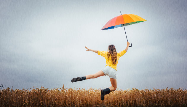 Frau freut sich &uuml;ber den Regen und springt mit dem Regenschirm in die Luft