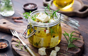 Fototapete Feta cheese marinated in olive oil with fresh herbs in glass jar. Wooden background. © annapustynnikova