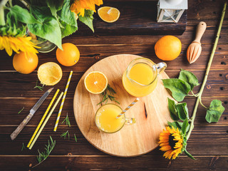 Glass of fresh pressed orange juice and oranges on wooden table. Autumn cozy rustic mood still life