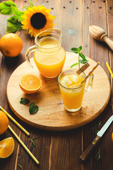 Glass of fresh pressed orange juice with ice cubes and oranges on wooden table. Autumn cozy rustic mood still life