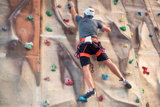 Young man practicing rock climbing on artificial wall indoors.