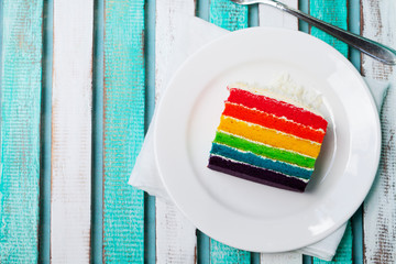 Rainbow cake on a white plate. Colorful wooden background. Top view. Copy space.