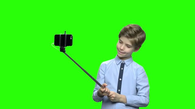 Little boy fooling around and making photos using selfie stick. Green hromakey background for keying.