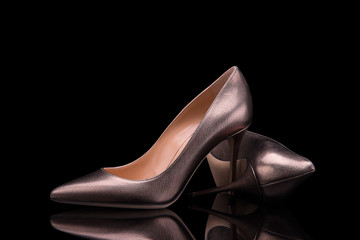 Elegant women's high heel shoes in bronze leather on a black background. Women's high-heeled shoes.