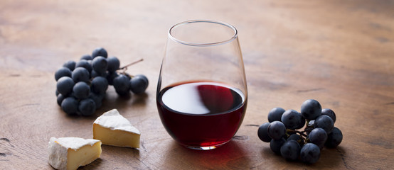 Glass of red wine with fresh grape and cheese on wooden table.