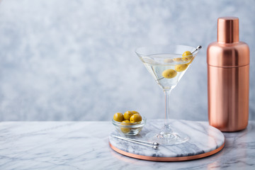 Martini cocktail with olives and bar shaker on marble table background. Copy space.