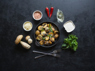 Rustic potatoes with mushrooms on a black table. Top view.