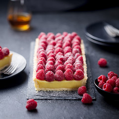 Raspberry tart with vanilla custard and white chocolate on slate board. Black stone background.