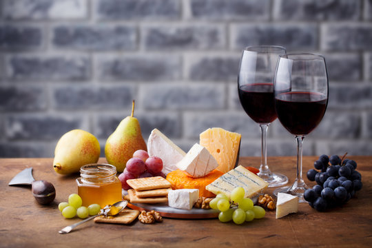 Assortment of cheese, grapes with red wine in glasses. Stone and wood background. Copy space.