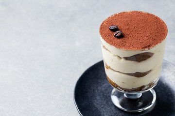Tiramisu, traditional Italian dessert in glass on a grey stone background. Copy space.