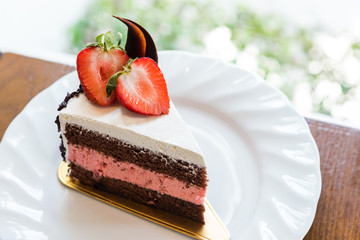 Closeup a piece of delicious strawberry cake on a white plate on wooden table. On wooden table with blur background