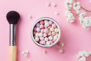 Pearl make up powder with white flowers and brush on pink pastel background. Top view.